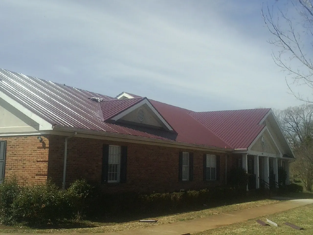 Red metal roof with gabled entries on a long brick building, from a Hail Damage Roof Repair job in Shaniko