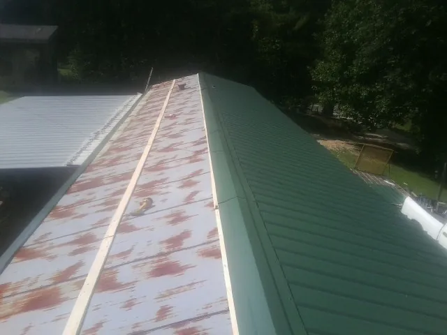 Old rusted panels beside newly installed green metal roofing — Wind Damage Roof Repair by Roofing Brothers in Shaniko