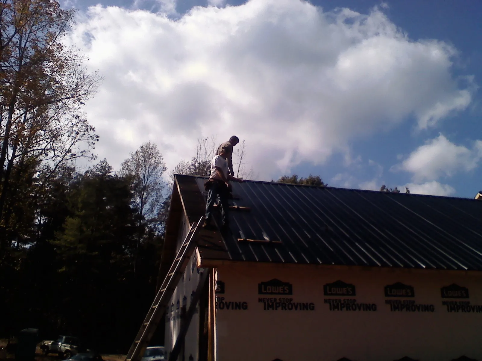 Roofer fastening dark metal panels high against a cloudy sky, from a Roof Inspection job in Shaniko