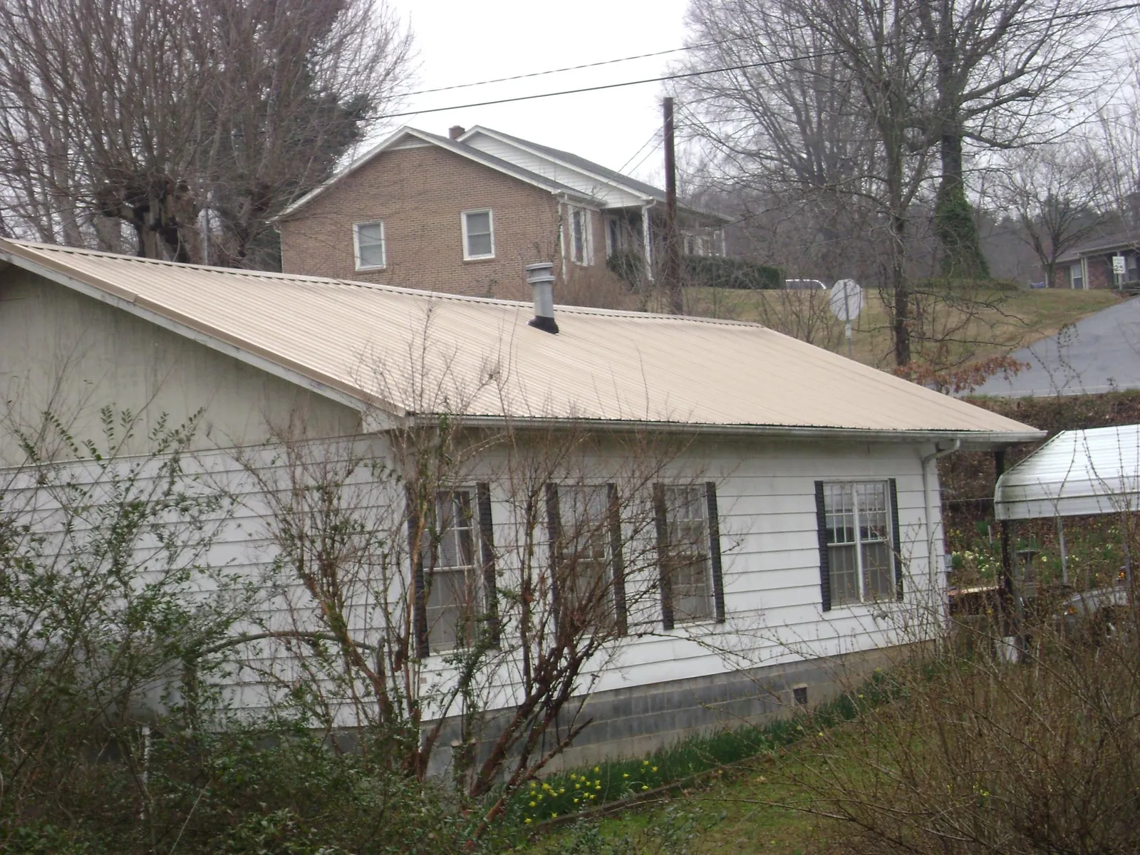 Tan metal roof on a white sided house set into a hillside — Commercial Roofing by Roofing Brothers in Shaniko